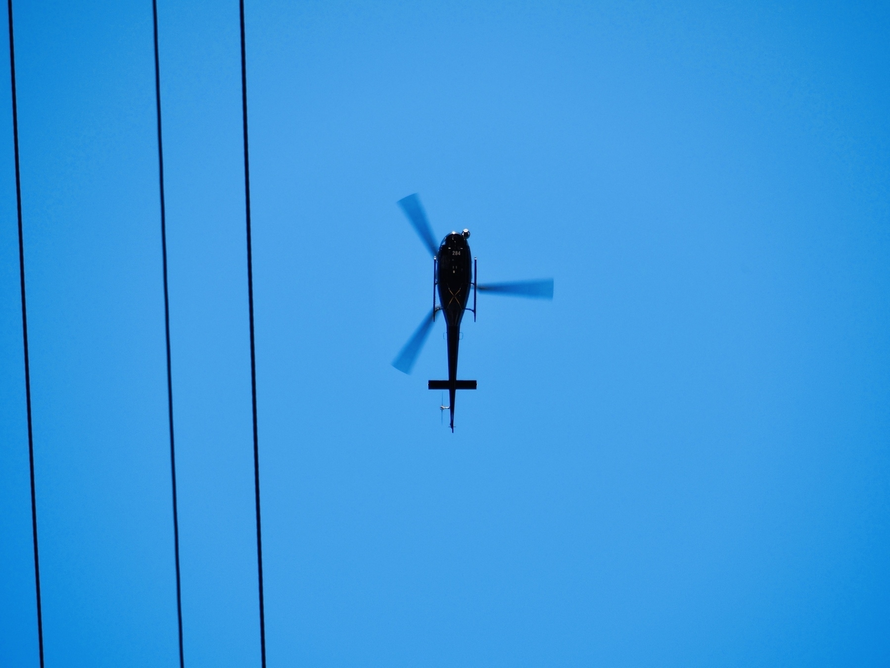 A helicopter flies overhead with power lines to the left of the frame.