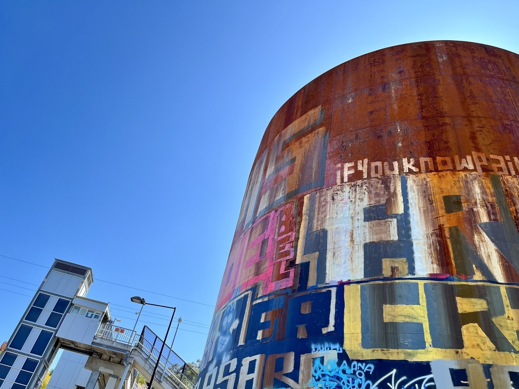 A railway lift shaft and staircase next to a rusty water tank against a blue sky