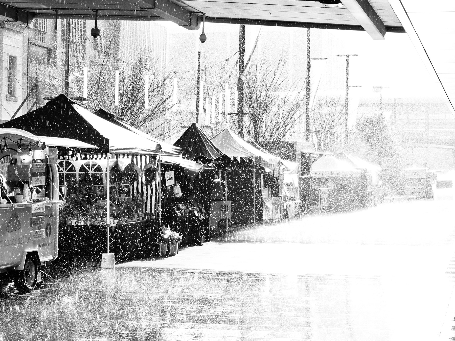 A row of market stalls in overexposed rain, with a walking bridge overhead