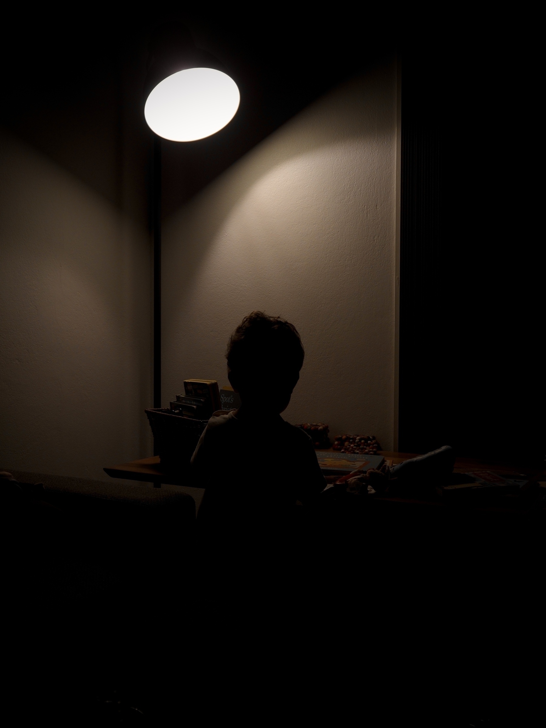 A silhouette of a child at a coffee table with books under a floor lamp