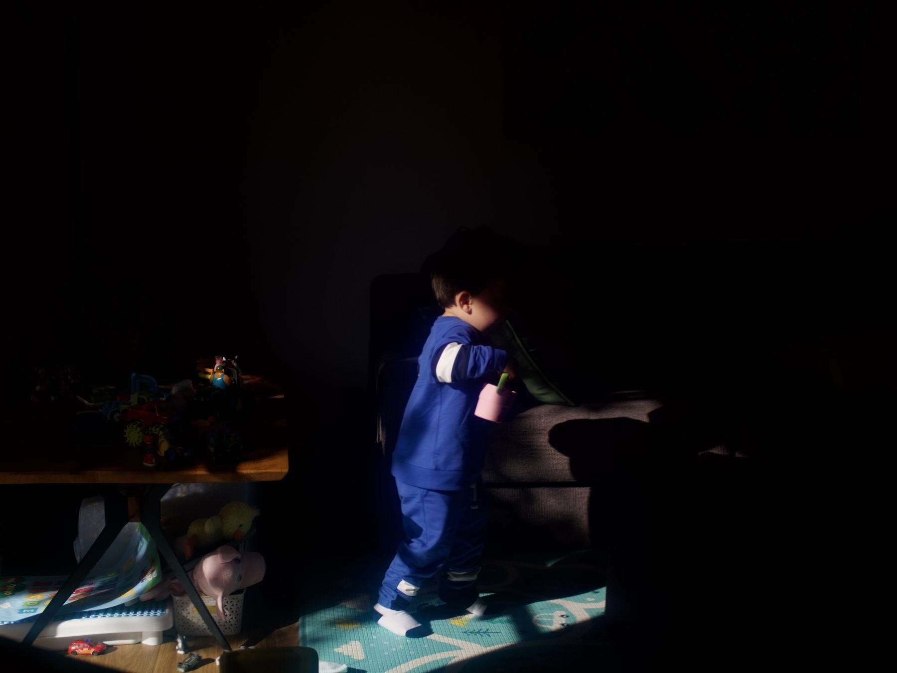A toddler runs across a lounge room, blanketed in shadow.