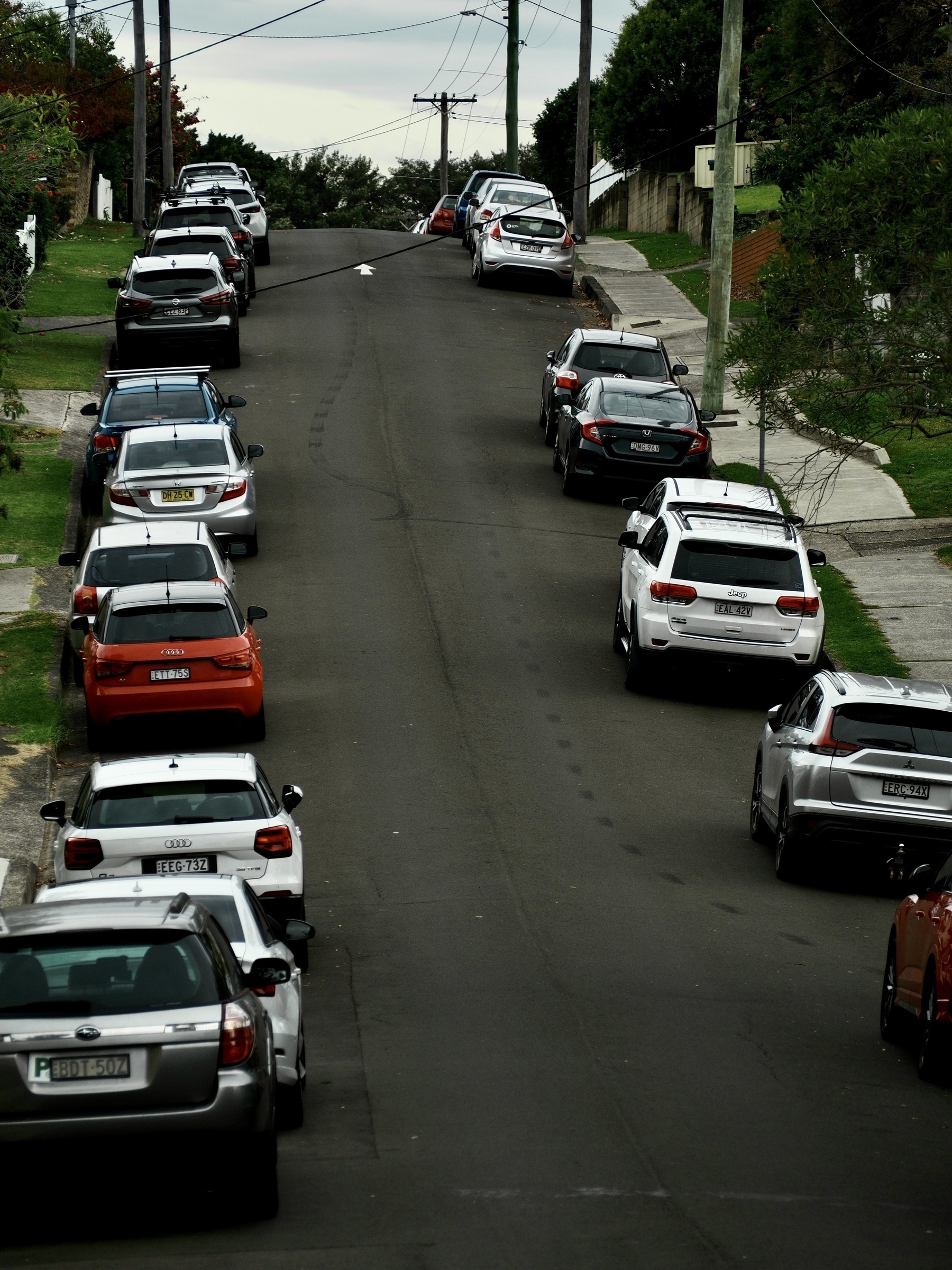 A suburban street on a hill, covered in cars and tyre marks