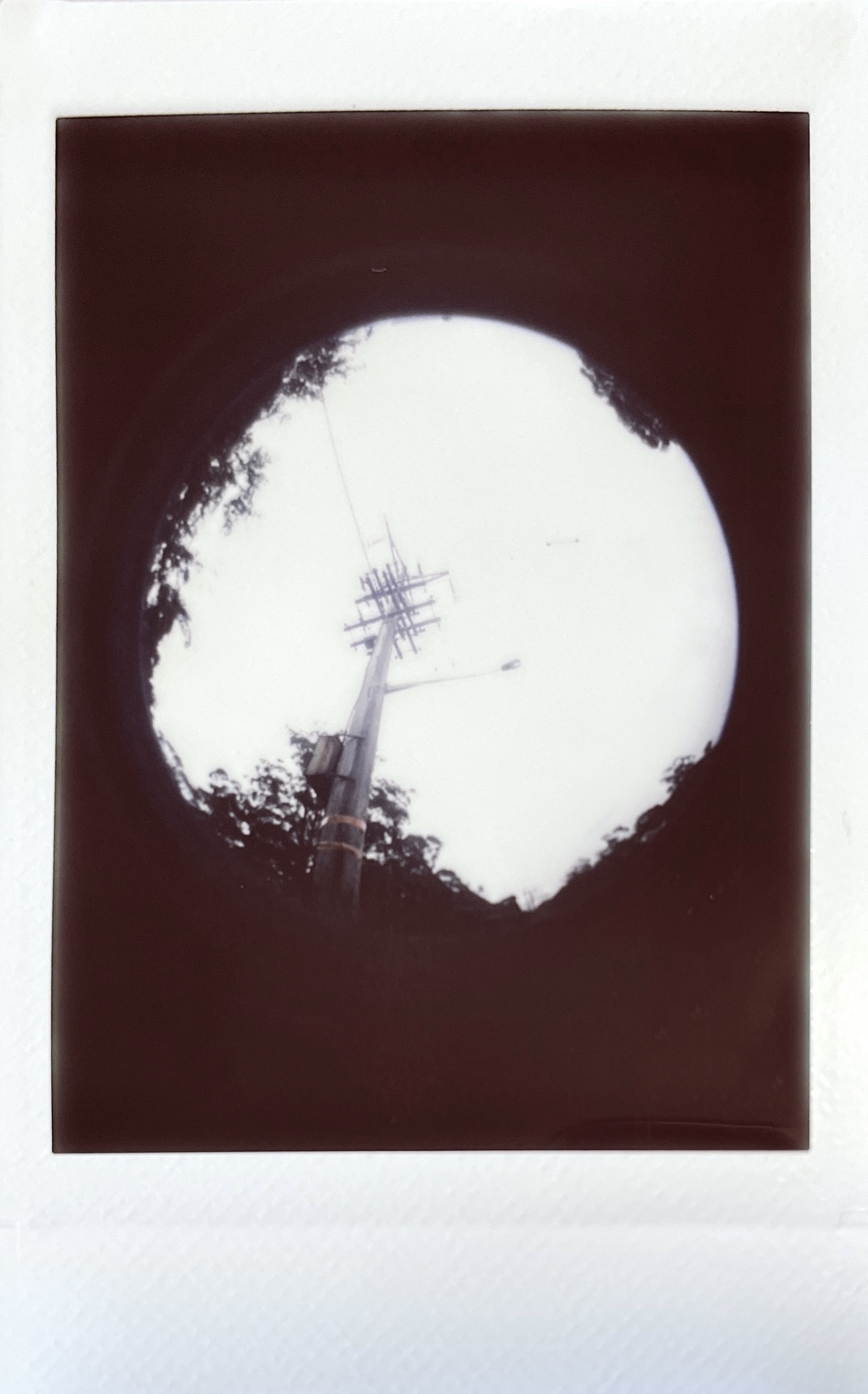 An instant photo looking up at a power line through a fisheye, creating the effect of a circle surrounded by darkness