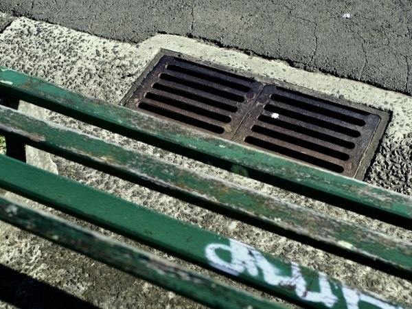 Looking down over a park bench and drain in a gutter