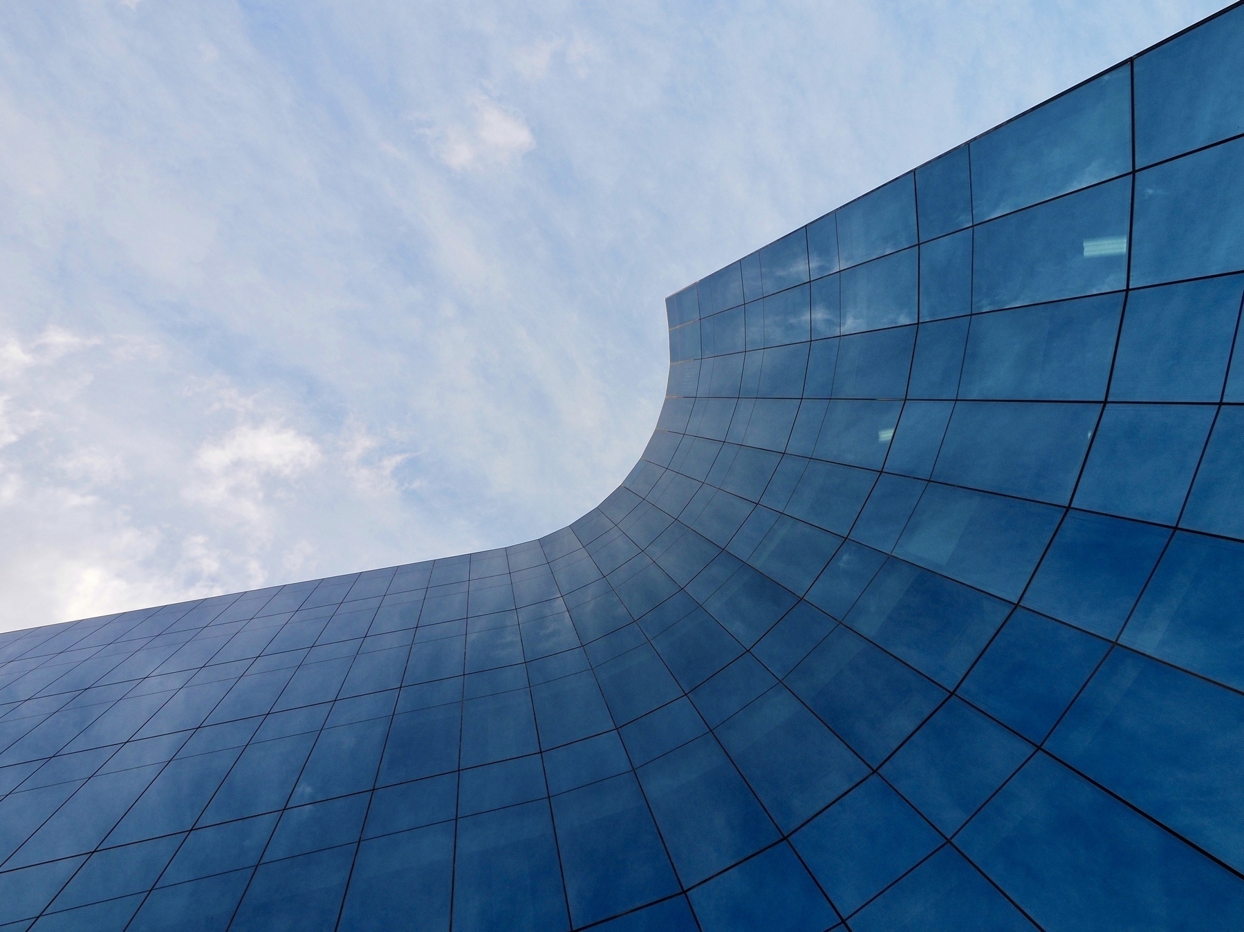 Looking up at a curved building with blue glass windows, with the sky above