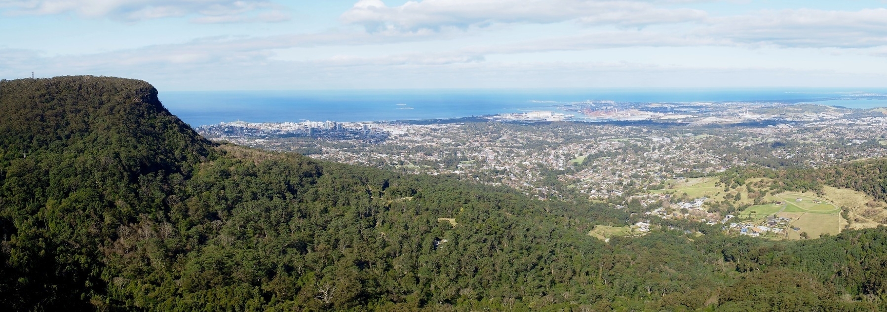 A wide landscape photo showing Geera (Mount Keira) and its foothills to the left, with the lower coastline of Wollongong and its surrounding hills as it stretches to the Tasman Sea