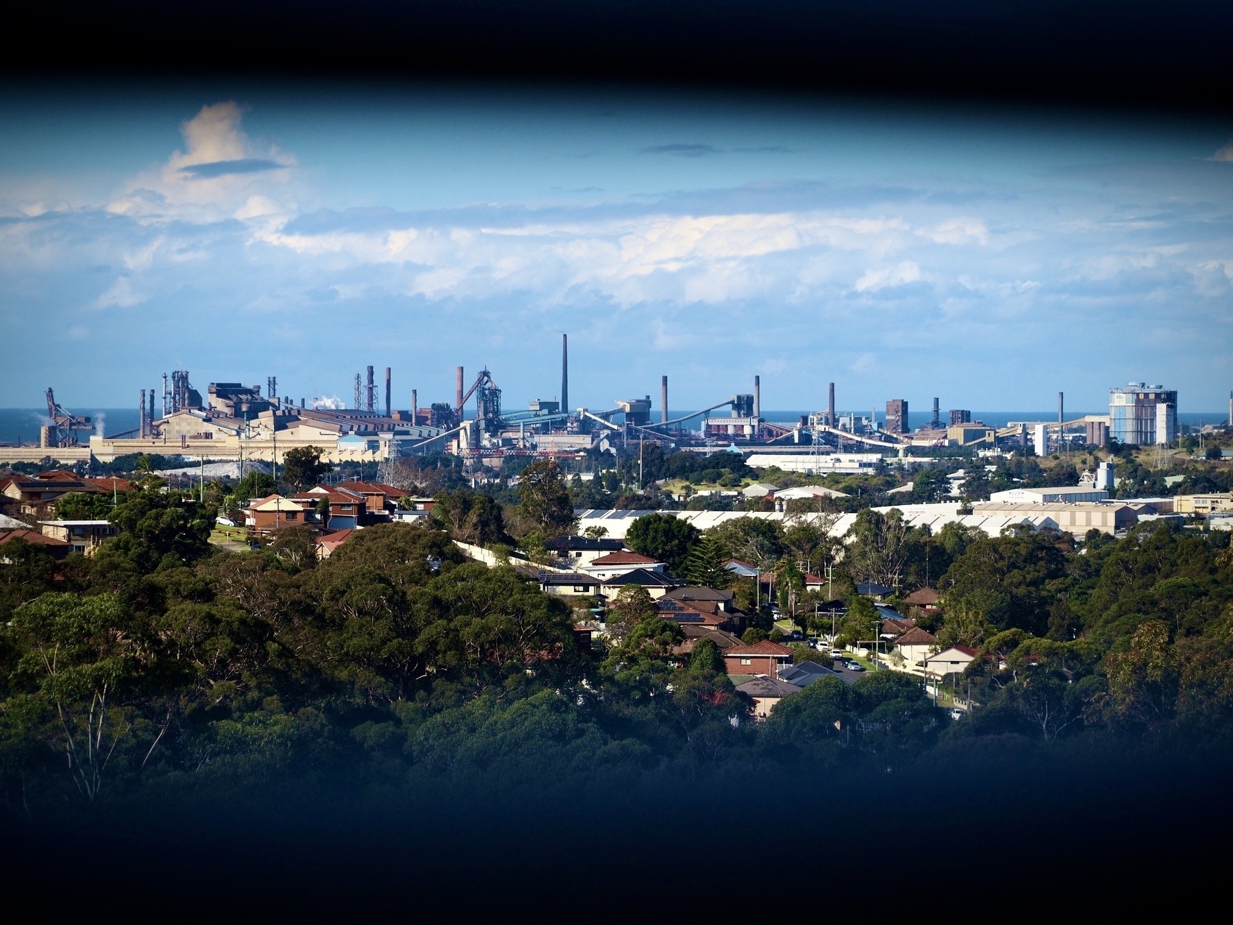 Looking at the Port Kembla Steelworks and surrounding leafy suburbs through window shutters, with the Tasman Sea in the very far distance