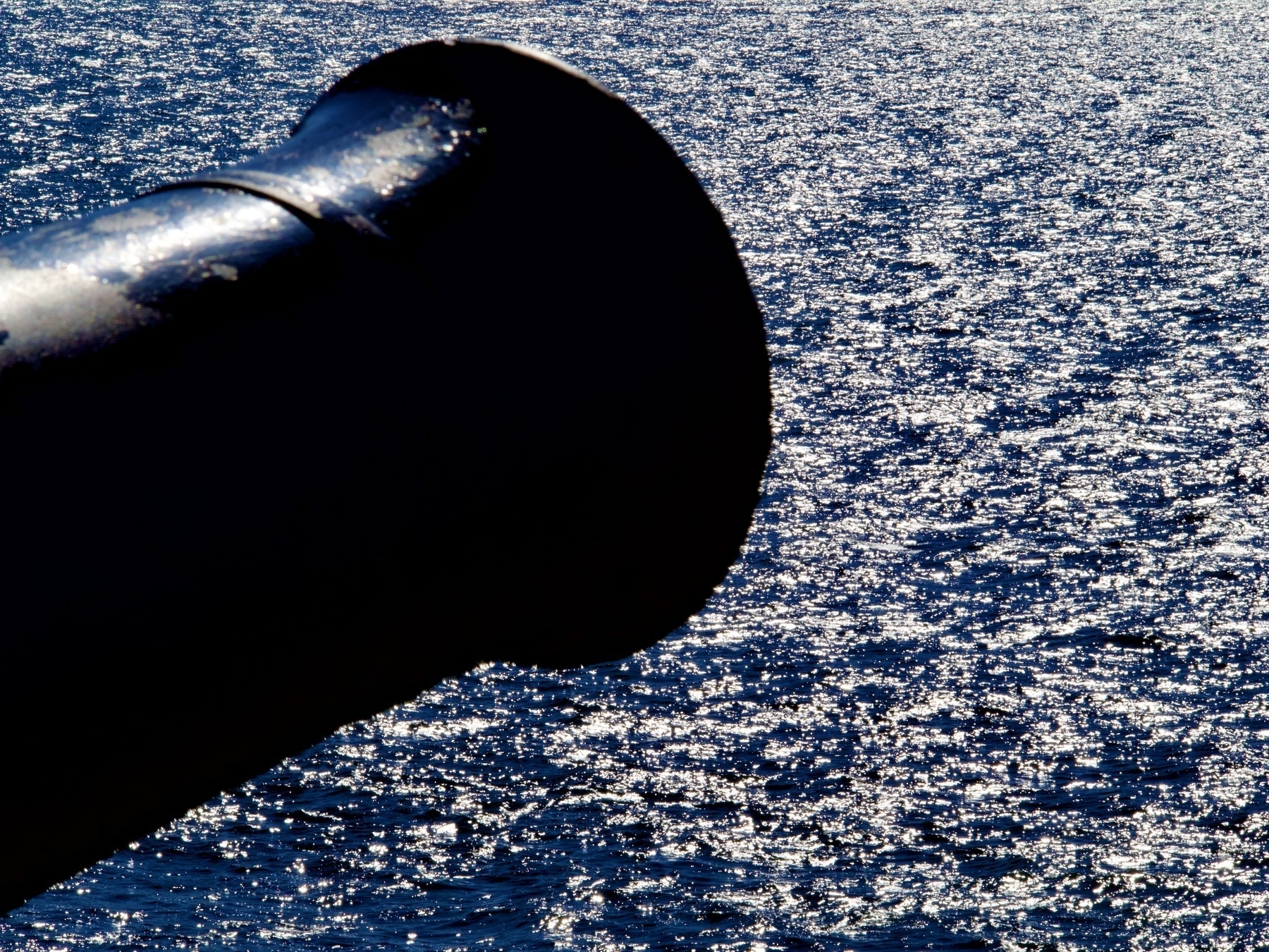 The silhouette of an old black cannon against the reflective surface of the ocean
