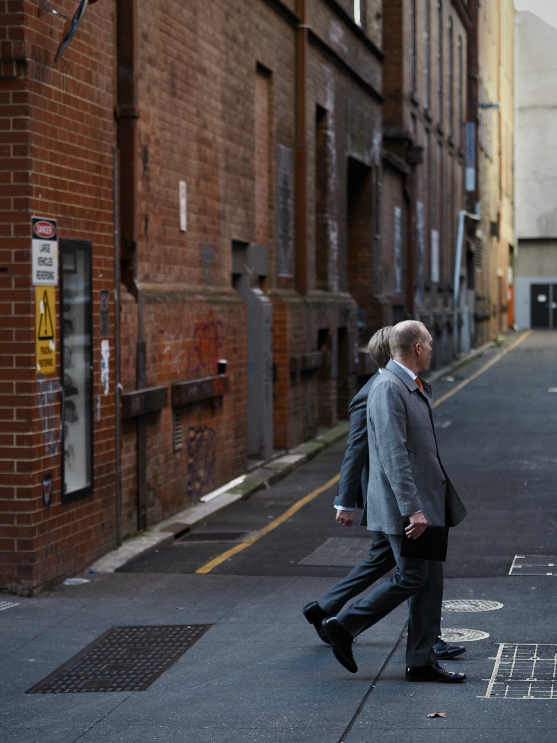 Two men in suits walk in sync past an alleyway.