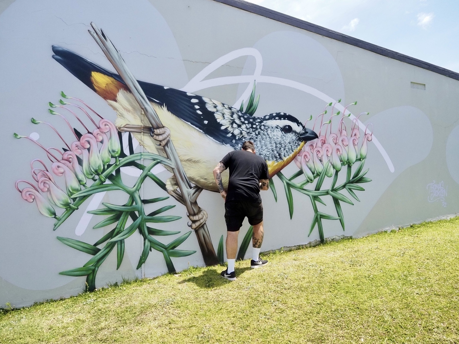 A street artist paints a picture of a bird on a branch.