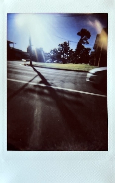 The Sun shines on a suburban intersection, with a blurred car entering the frame from the right-hand side.